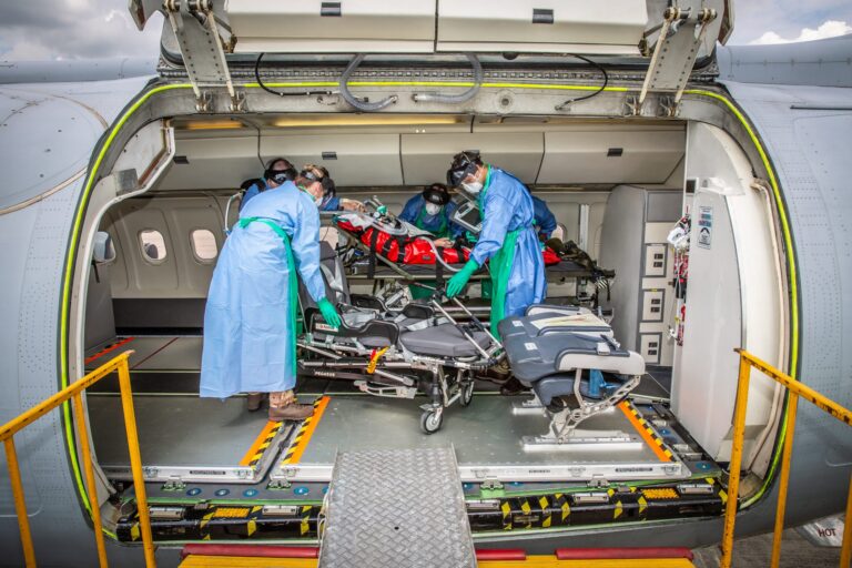 Medical personnel in protective gear load a veteran on a stretcher into an airplane equipped for military medical transport.