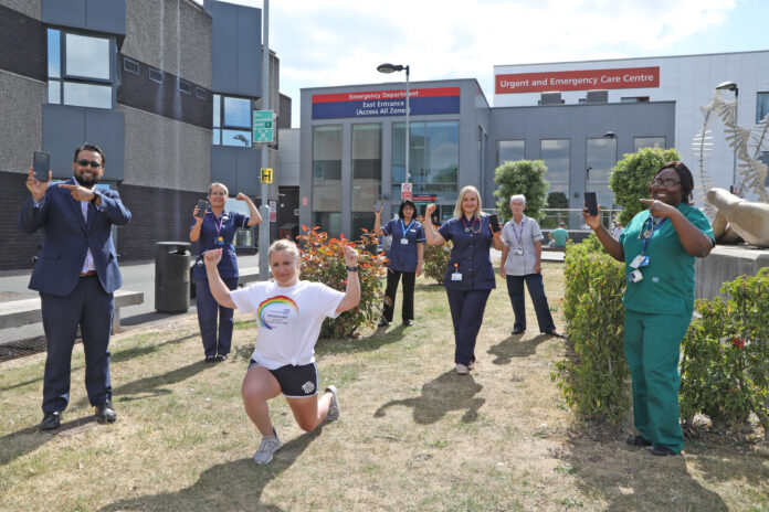 A group of healthcare workers and one person in a white t-shirt, possibly involved in Army resettlement, pose outside a hospital's emergency department, smiling and holding tablets.