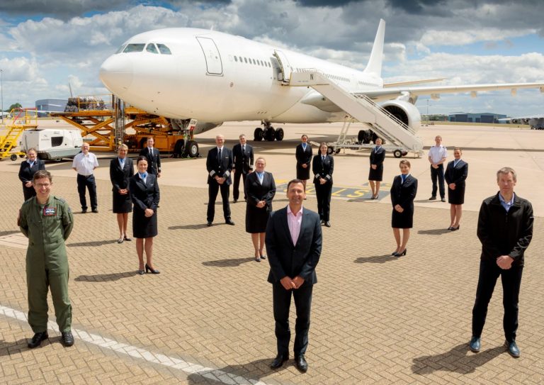 A group of airline staff, including pilots and cabin crew, stand spaced apart in front of a large white airplane on the airport tarmac, resembling a Pathfinder team ready for an important mission.