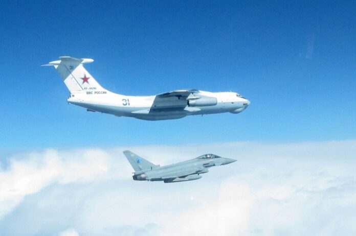 A Russian military aircraft soars above a grey army jet, set against a backdrop of blue sky and clouds—a striking tribute to veteran service in the armed forces.