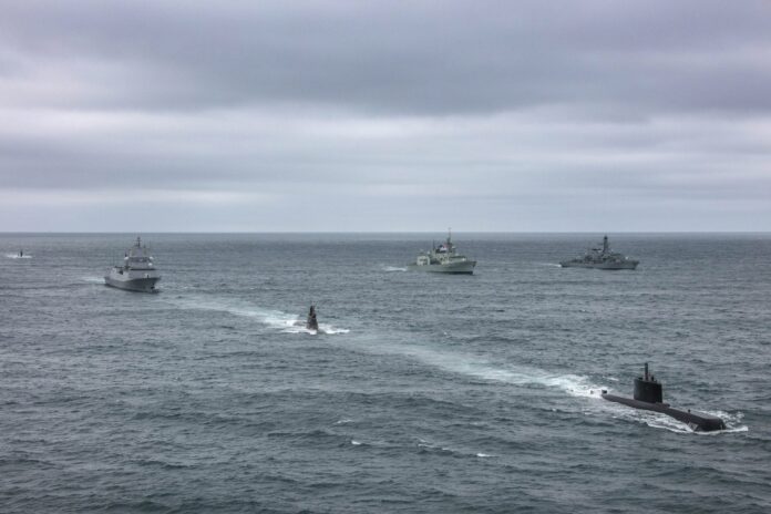 Four naval ships, including two submarines and two surface vessels, travel in formation on the open ocean under a cloudy sky—each a pathfinder in the proud tradition of veteran sailors.