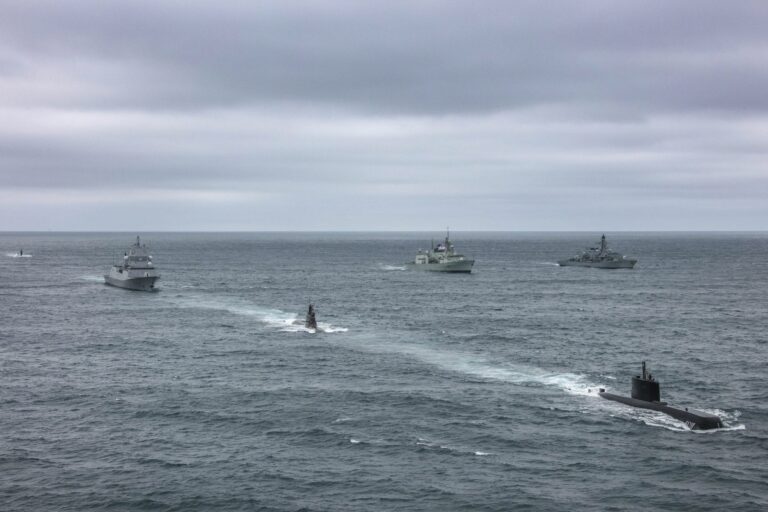 Four naval ships, including two submarines and two surface vessels, travel in formation on the open ocean under a cloudy sky—each a pathfinder in the proud tradition of veteran sailors.