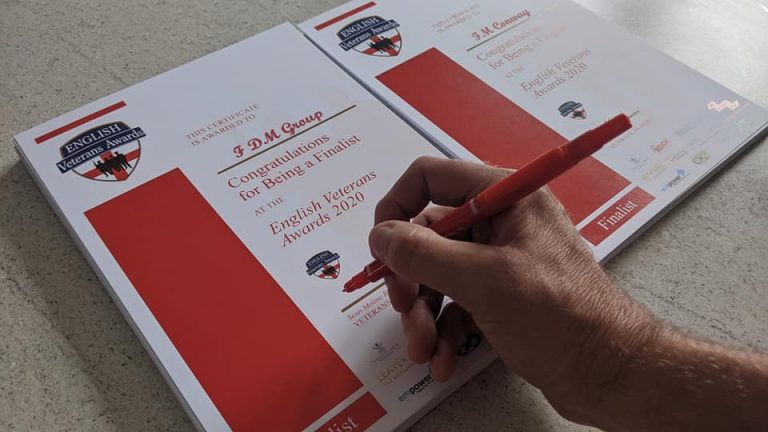 A hand holding a red pen prepares to sign a finalist certificate for the English Veterans Awards 2021, honoring remarkable Army and military resettlement achievements, on a light-colored table.