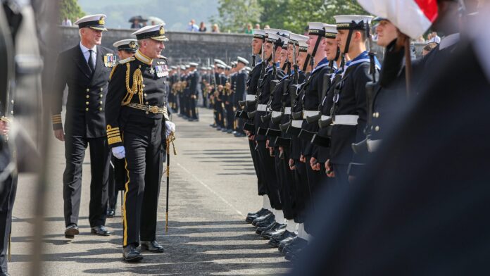 A senior Pathfinder naval officer in a decorated uniform inspects a row of sailors standing at attention during a formal outdoor military ceremony.