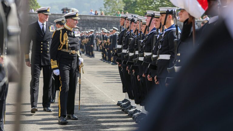 A senior Pathfinder naval officer in a decorated uniform inspects a row of sailors standing at attention during a formal outdoor military ceremony.