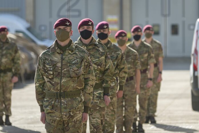 A group of Pathfinder soldiers in camouflage uniforms and maroon berets stand in a line outdoors, all wearing black or green face masks.