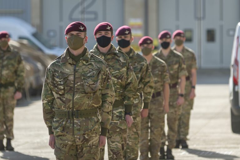 A group of Pathfinder soldiers in camouflage uniforms and maroon berets stand in a line outdoors, all wearing black or green face masks.