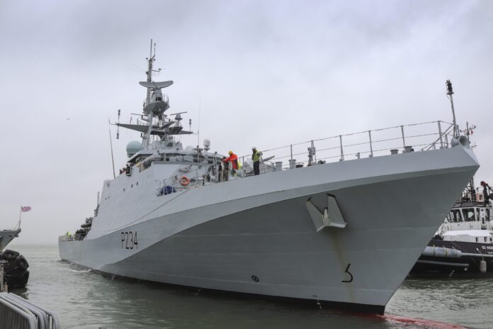 A gray Royal Navy patrol vessel with the identifier P284 is docked at a pier, with several crew members in safety gear visible on the deck.