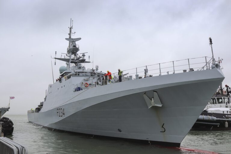 A gray Royal Navy patrol vessel with the identifier P284 is docked at a pier, with several crew members in safety gear visible on the deck.