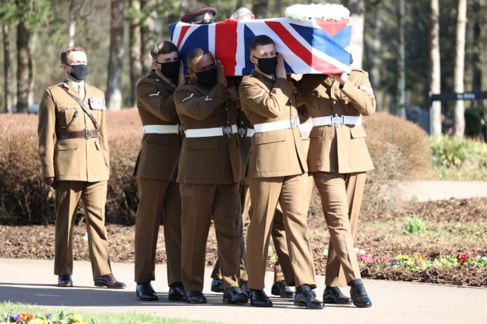 A group of uniformed Army soldiers carry a flag-draped coffin outdoors during a formal military procession.