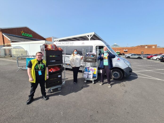 Three people stand by a van in a parking lot, posing with carts of food and supplies, with an ASDA store visible in the background, wearing Army Pathfinder uniforms.