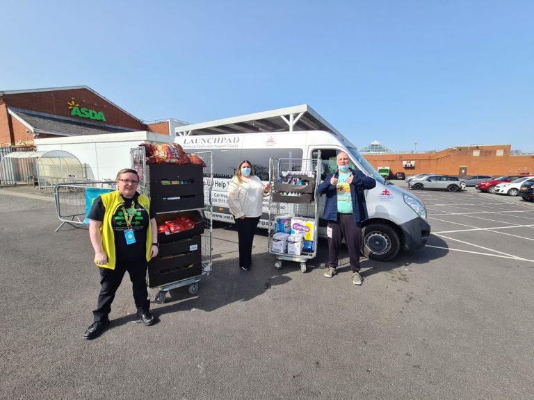 Three people stand by a van in a parking lot, posing with carts of food and supplies, with an ASDA store visible in the background, wearing Army Pathfinder uniforms.