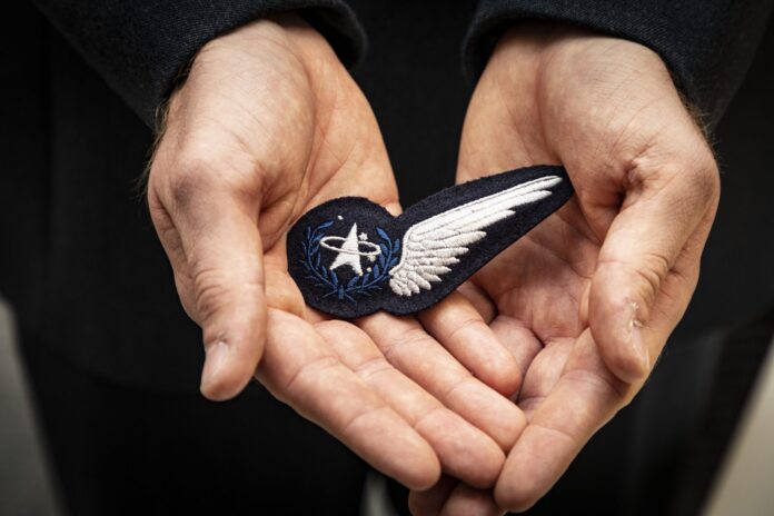 A person holds a cloth badge featuring an embroidered white wing and a NASA logo in both hands, symbolizing a veteran’s journey of resettlement after service in the Royal Navy.