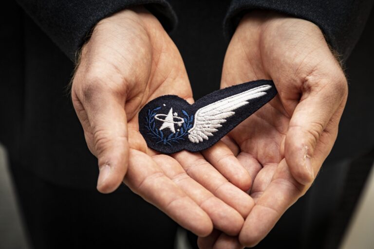 A person holds a cloth badge featuring an embroidered white wing and a NASA logo in both hands, symbolizing a veteran’s journey of resettlement after service in the Royal Navy.