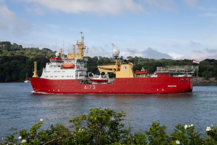 A large red research vessel marked A173, possibly serving as a military Pathfinder, sails on a river with green trees and a partly cloudy sky in the background.