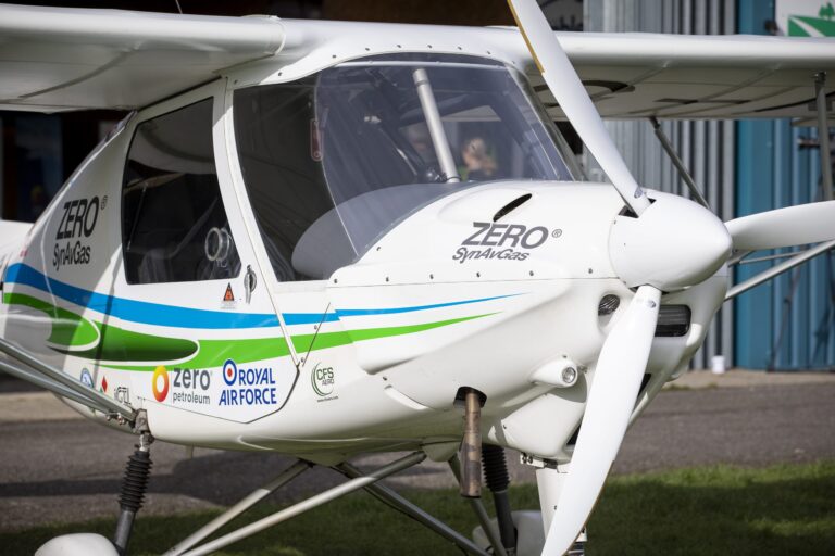 Close-up view of the nose and cockpit of a small, single-engine Pathfinder airplane, with "ZERO Syn2Gas" and various sponsor logos on its fuselage.