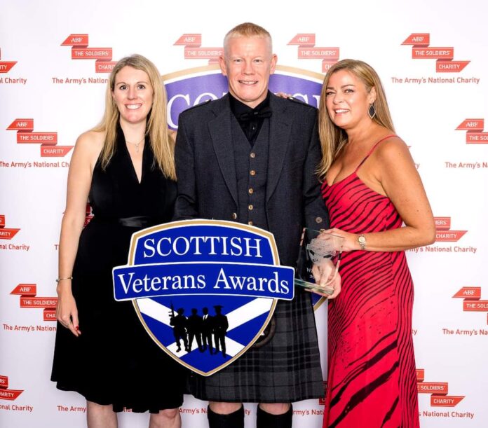 Three people pose together at the Scottish Veterans Awards, celebrating military resettlement success. One holds a trophy, another a large event sign, and a branded Pathfinder backdrop completes the scene.