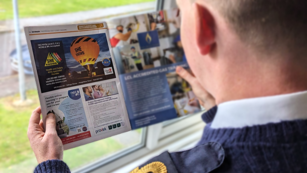 A person in a blue sweater reads a magazine, focusing on a page featuring an advertisement for hot air balloon rides and considering the Health & Safety measures involved.