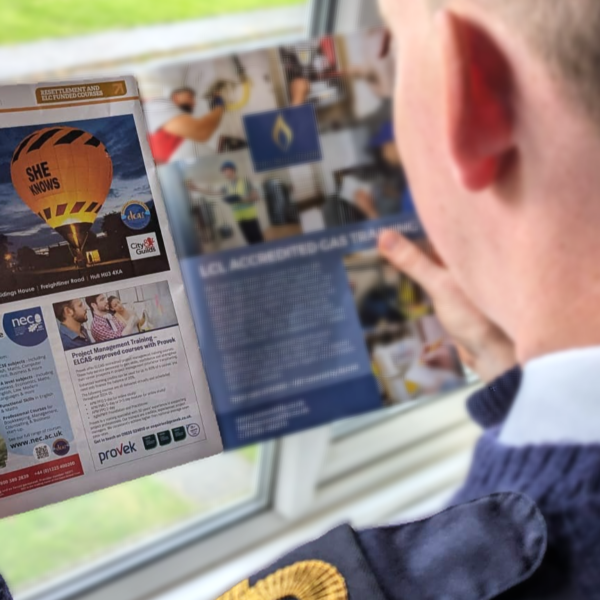 A person in a blue sweater reads a magazine, focusing on a page featuring an advertisement for hot air balloon rides and considering the Health & Safety measures involved.