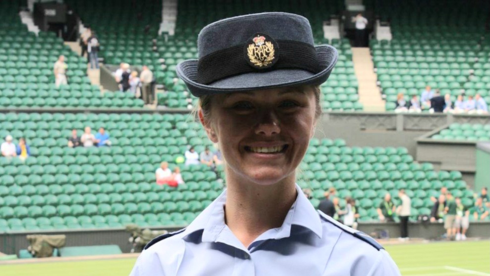 A person in a uniform with a hat featuring a badge is smiling, standing in a stadium with green seats, embodying the spirit of helping through their support for the Royal British Legion.