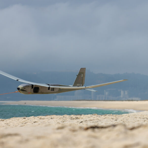 Under a cloudy sky on a sandy beach, a soldier from the Royal Navy operates an uncrewed drone vessel.