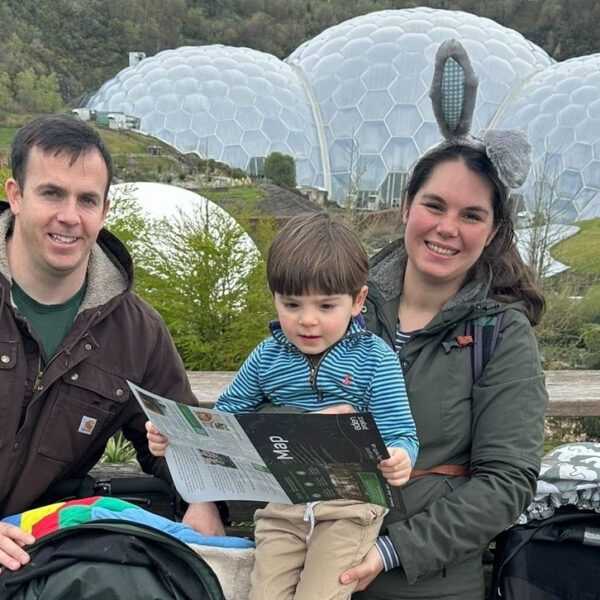 A military family of three poses outdoors, with a child holding a map. Behind them, geodesic domes stand as beacons of hope amidst the lush greenery.