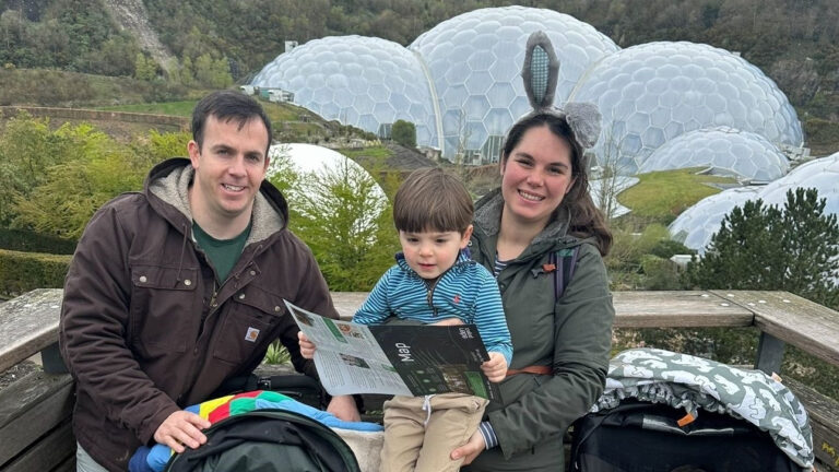 A military family of three poses outdoors, with a child holding a map. Behind them, geodesic domes stand as beacons of hope amidst the lush greenery.