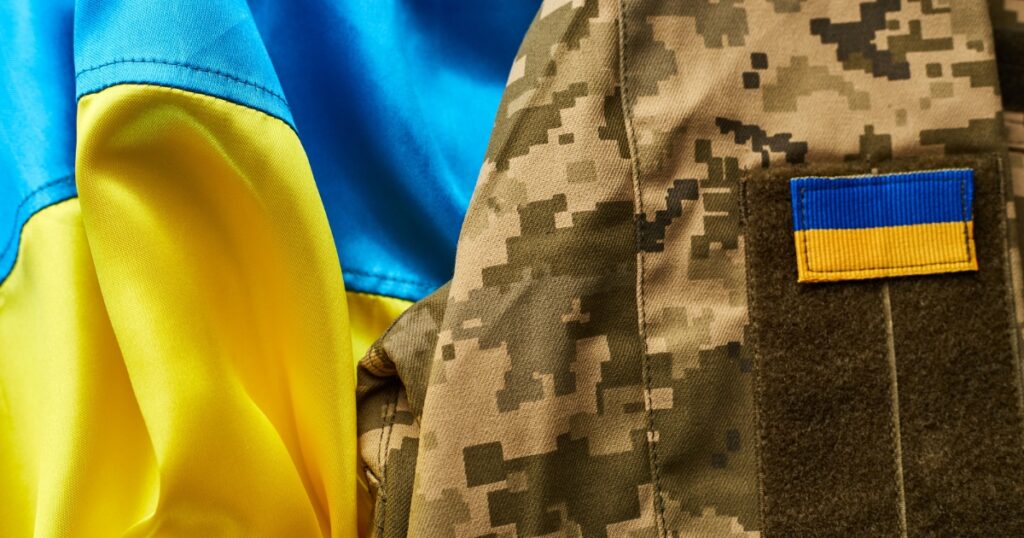 Close-up of a yellow and blue flag, symbolizing Kyiv's spirit, fluttering next to a camouflage uniform with a matching patch.