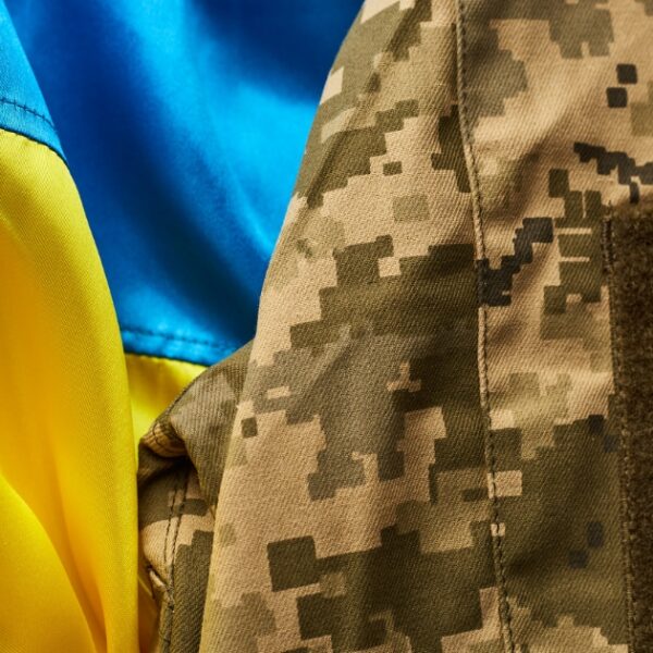 Close-up of a yellow and blue flag, symbolizing Kyiv's spirit, fluttering next to a camouflage uniform with a matching patch.