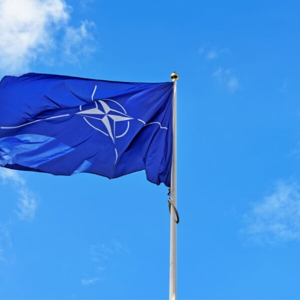 The NATO flag waves proudly on a flagpole against a clear blue sky, as UK troops participate in a significant NATO exercise in Eastern Europe.