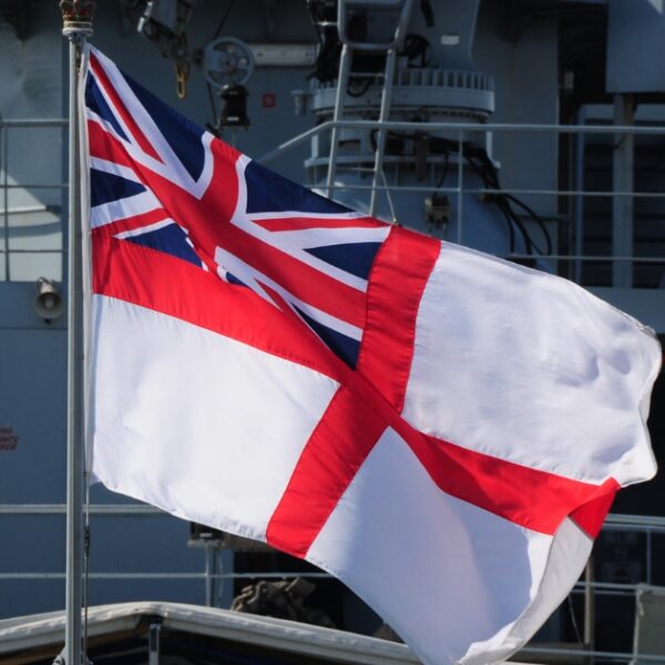 A white flag with a red cross and a Union Jack in the corner is flying on a naval warship, marking a significant milestone in its journey.