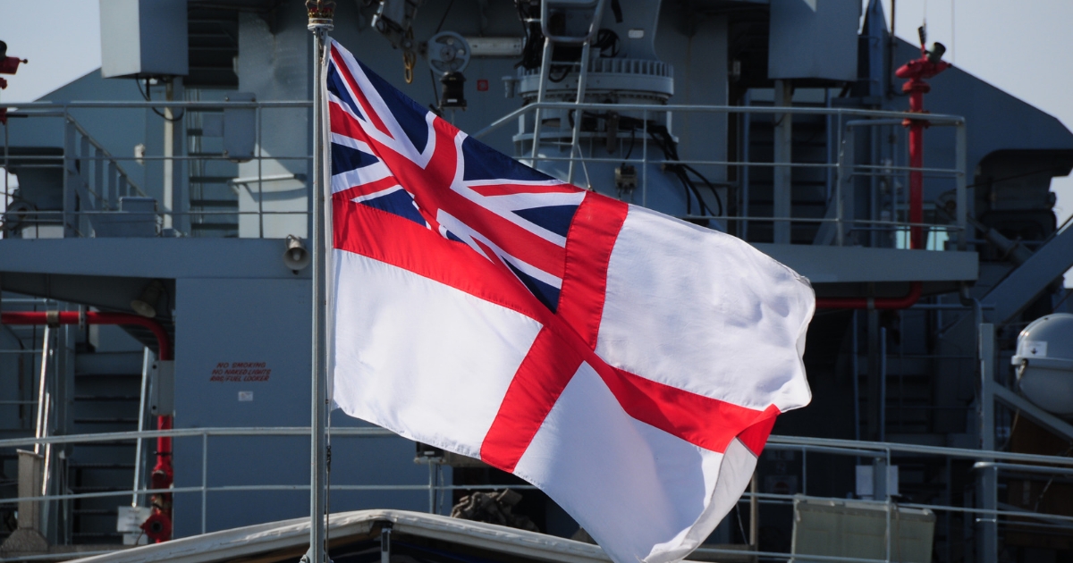 A white flag with a red cross and a Union Jack in the corner is flying on a naval warship, marking a significant milestone in its journey.