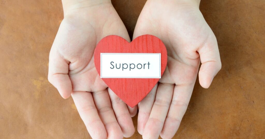 Hands holding a red heart with the word "Support" on it, symbolizing the RAF Veteran’s Hub initiative, placed on a brown background.