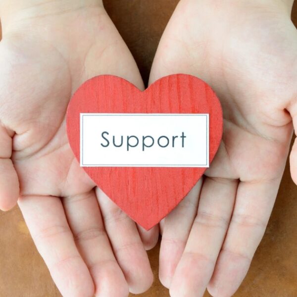 Hands holding a red heart with the word "Support" on it, symbolizing the RAF Veteran’s Hub initiative, placed on a brown background.