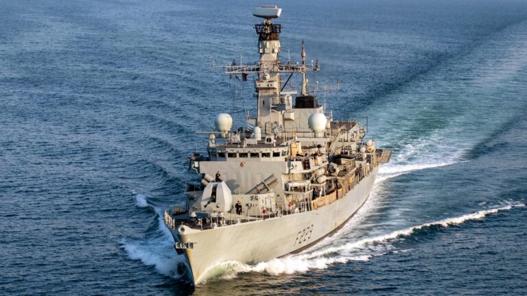 The HMS Lancaster sails through calm waters in the Middle East, with visible antennas and equipment on deck.