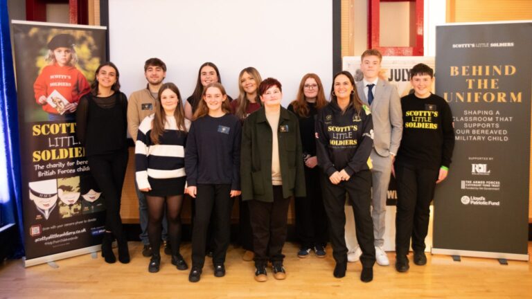 A group of people stands before a "Scotty's Little Soldiers" backdrop, flanked by promotional banners. Their presence highlights the urgent need for support dedicated to bereaved military children.