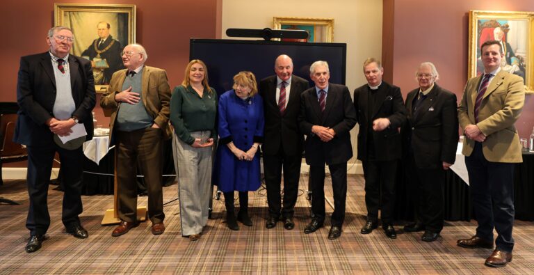 Eight adults in business attire stand side by side indoors in front of a large screen, with framed portraits behind them, following a military fundraiser attended by the Chief of the General Staff.