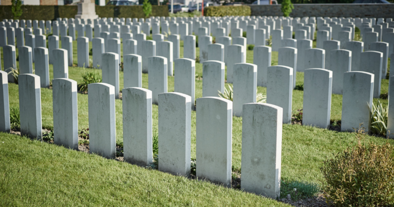 Rows of uniform white gravestones in a cemetery, honoring those supported by the Veterans' Foundation, with green grass and trimmed hedges in the background.
