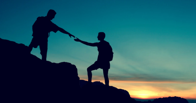 Silhouettes of two hikers on a rocky slope at sunset, with one person reaching down to help the other up—a powerful symbol of support for veterans overcoming suicidal behaviours.