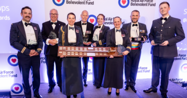 Eight people in formal military attire stand on stage holding trophies and a large award plaque at the RAF Benevolent Fund Awards, celebrating this year’s Awards Winners.