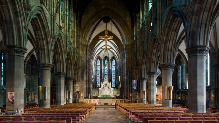 Interior view of a large, gothic-style church in Edinburgh with vaulted ceilings, stained glass windows, stone arches, and rows of empty pews facing an ornate altar—perfect for SSAFA events or free tickets to special performances.