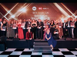A large group of people in formal attire pose on stage holding certificates at the BFA HSBC UK British Franchise Awards event, celebrating the best in franchising.