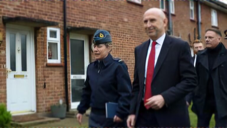 A uniformed officer and a man in a red tie walk outside a brick building, accompanied by others—highlighting efforts to improve military housing and support programs like Homes for Heroes for service members and their families.