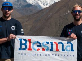 Two men wearing sunglasses and Blesma t-shirts, both amputees, hold a Blesma banner in front of a mountainous landscape during their inspiring Bhutan trek.