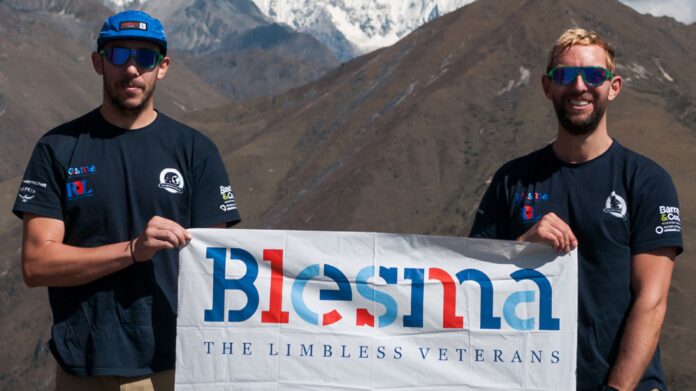 Two men wearing sunglasses and Blesma t-shirts, both amputees, hold a Blesma banner in front of a mountainous landscape during their inspiring Bhutan trek.