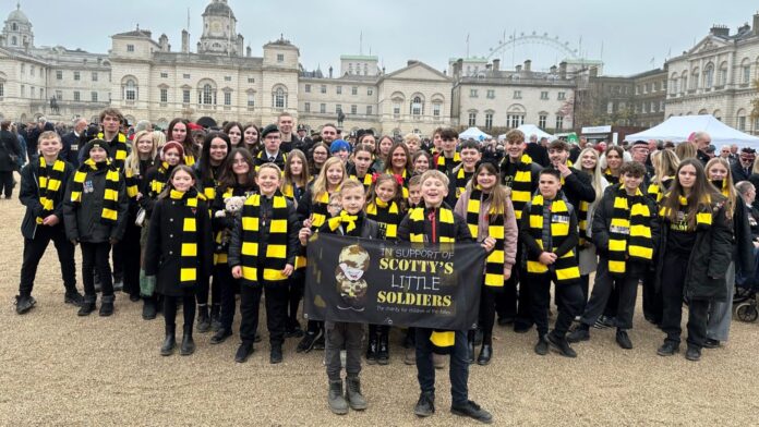 A large group of military children and teens, many wearing black and yellow scarves, stand together holding a 