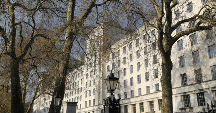 Leafless trees and black lampposts line the street in front of a large, white multi-story building with many windows—a serene spot where Veterans may find connection through a UK support network on a clear day.