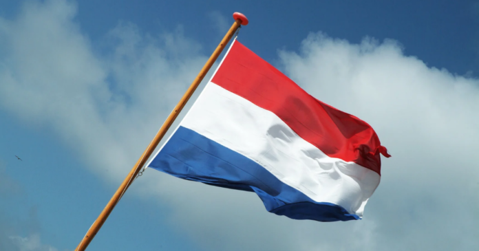A red, white, and blue horizontal tricolor flag on a wooden pole flying against a partly cloudy blue sky, representing the spirit of Taxi Charity and celebrating its recent Royal Honour.