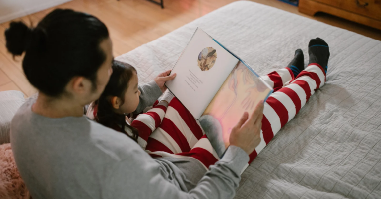 An adult and a child, both in striped pajamas, sit on a bed reading a picture book together, sharing the joy of kids reading before bedtime.