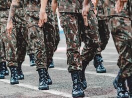A group of UK Armed Forces personnel in camouflage uniforms and black boots march in formation on a paved surface.